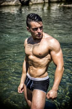 Handsome, hot young bodybuilder shirtless in trunks, in the sea showing his muscular torso and arms