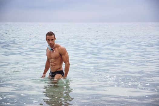 Handsome, hot young bodybuilder and swimmer in the sea showing his muscular torso and arms