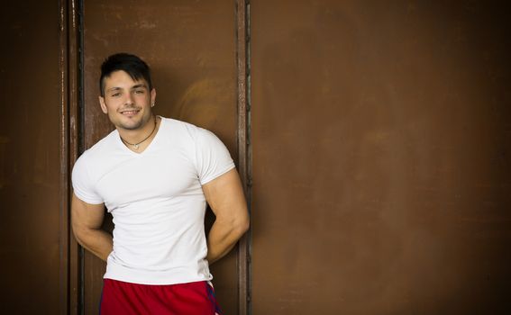 Muscular young man portrait indoors smiling at camera, wearing white t-shirt