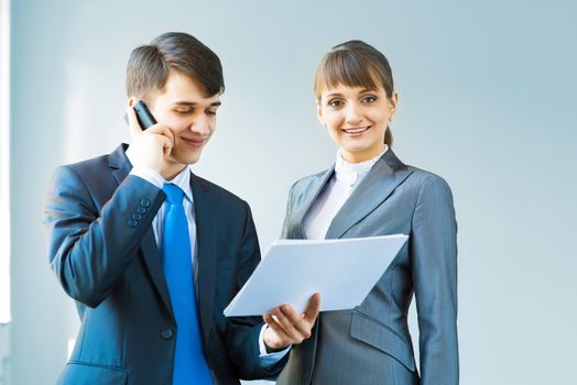 two business partners discussing documents, the man speaks on a cellular telephone