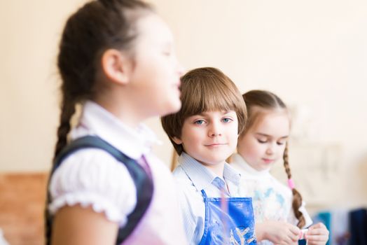 boy draws in the classroom with the other children, the children stand in a row in the table