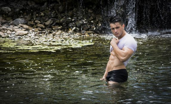 Handsome, hot young bodybuilder in the sea or river showing his muscular abs and arms
