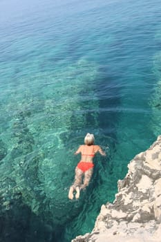 Lady entering the sea between sharp rocks