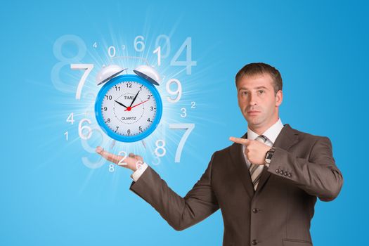 Businessman in a suit hold alarm clock with figures on blue background 