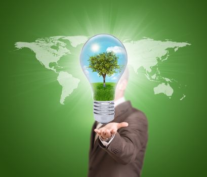 World map. Businessman in a suit hold bulb with tree and landscape