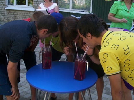 Teenagers drink juice from tall glasses as a competition for speed