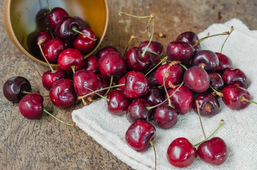 fresh organic cherries spilling out from the bowl  on wooden table  background