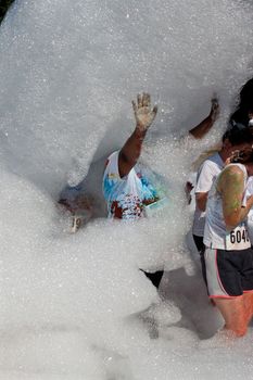 Lawrenceville, GA, USA - May 31, 2014:  A triumphant woman raises her arms while walking through an avalanche of bubbles and foam at Bubble Palooza.