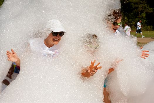 Lawrenceville, GA, USA - May 31, 2014:  Women smile and laugh while emerging from a cloud of foamy soap suds at Bubble Palooza.