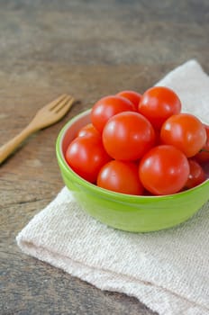 Red cherry tomatoes in green bowl  on a textured  wooden background