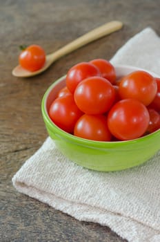 Red cherry tomatoes in green bowl and wooden spoon