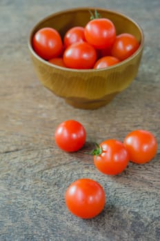 Red cherry tomatoes in bowl and  on a textured  wooden background