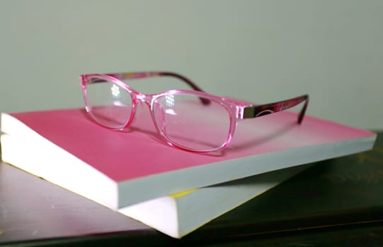 The  eye glasses is on the pink and yellow books.