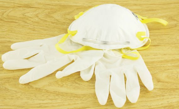 N95 white mask and gloves for disease prevention, placed on wooden floor.                                