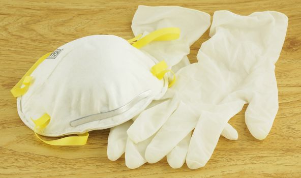 N95 white mask and gloves for disease prevention, placed on wooden floor.                                