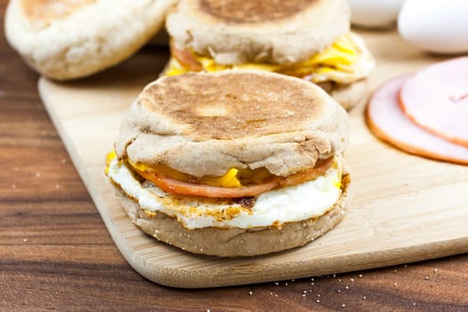 English muffin, egg, ham, and cheese breakfast sandwich on a cutting board with ingredients in the background.