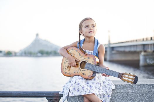 Small infant girl playing guitar in the city