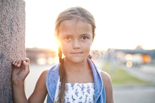 Smiling child standing near the wall in evening sun