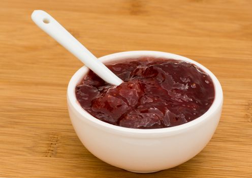 Small pot of strawberry Jam on a wooden board 