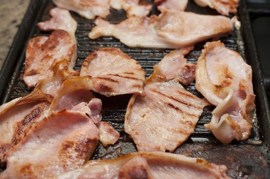 Delicious lean grilled rashers of smoked bacon on a griddle for a family breakfast or in a restaurant, close up high angle view