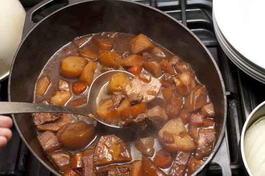 Delicious beef stew with carrots and potatoes in a rich gravy in a pot with a ladle for serving
