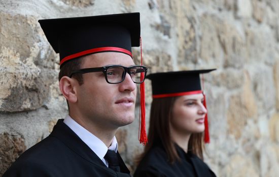 Portrait of a young couple in the gradution day posing near a stoned wall. Selective focus on the man.