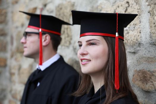 Portrait of a young couple in the gradution day posing near a stoned wall. Selective focus on the woman.