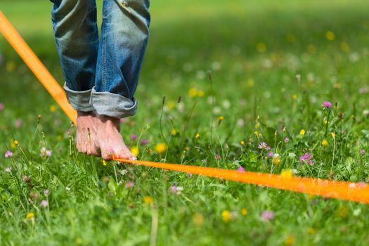 Guy practising slack line in the city park. Slacklining is a practice in balance that typically uses nylon or polyester webbing tensioned between two anchor points.