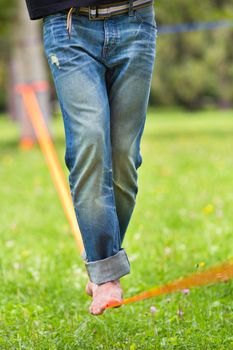 Guy practising slack line in the city park. Slacklining is a practice in balance that typically uses nylon or polyester webbing tensioned between two anchor points.