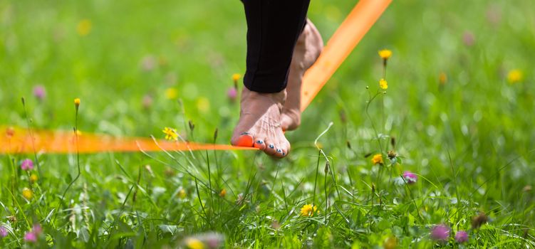 Lady practising slack line in the city park. Slacklining is a practice in balance that typically uses nylon or polyester webbing tensioned between two anchor points.