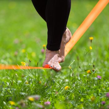 Lady practising slack line in the city park. Slacklining is a practice in balance that typically uses nylon or polyester webbing tensioned between two anchor points.