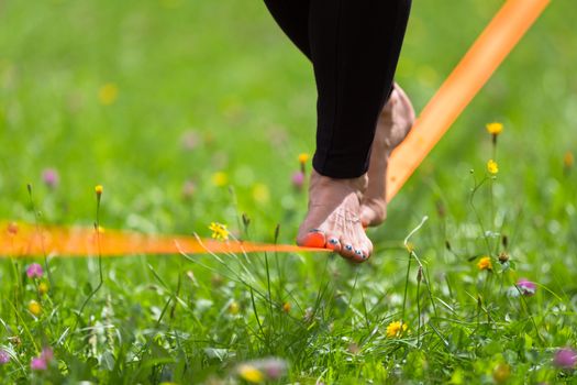 Lady practising slack line in the city park. Slacklining is a practice in balance that typically uses nylon or polyester webbing tensioned between two anchor points.