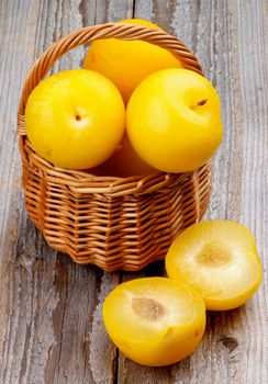 Ripe Sweet Yellow Plums in Wicker Basket and Halves isolated on Rustic Wooden background