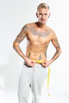Attractive man measuring waist wearing sweatpants on a white background