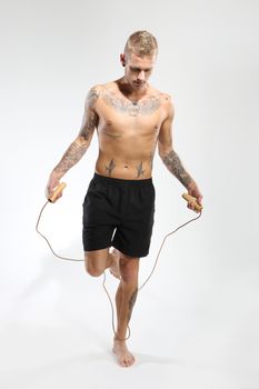 Attractive young boy jumping rope, tattooed in sports trousers