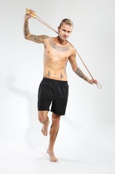 Attractive young boy jumping rope, tattooed in sports trousers