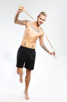 Attractive young boy jumping rope, tattooed in sports trousers