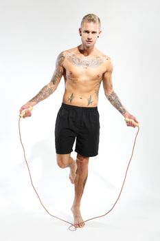 Attractive young boy jumping rope, tattooed in sports trousers