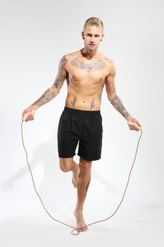 Attractive young boy jumping rope, tattooed in sports trousers