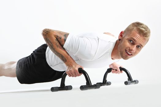 Attractive young man doing push-ups, tattooed in sports trousers