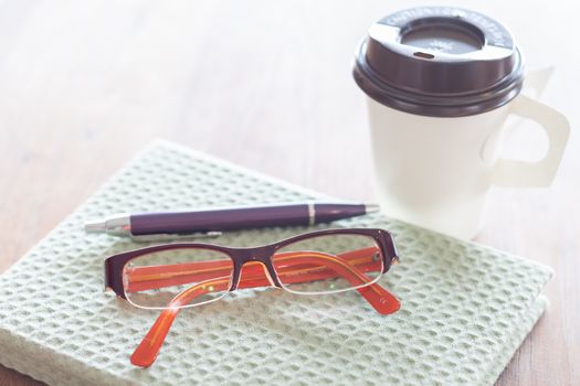 Notebook, pen eyeglasses and coffee cup on wooden table, stock photo