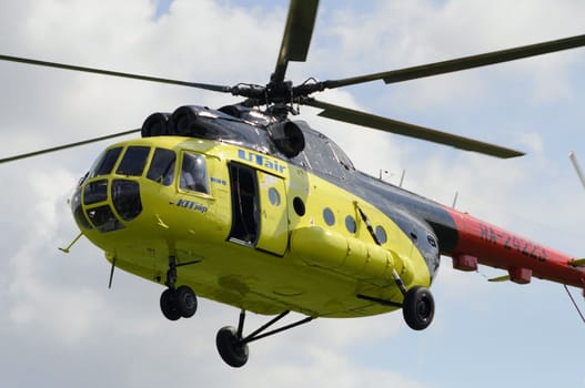 The yellow MI-8 helicopter flies against clouds with an open door