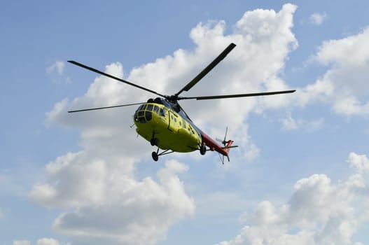 The yellow MI-8 helicopter flies against clouds