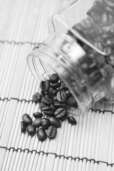 Coffee beans spilled from glass bottle on a wooden table top.