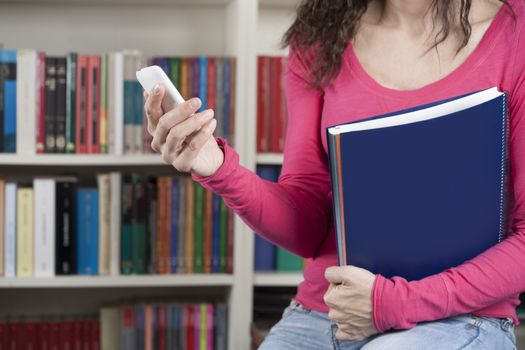 woman student with pink jersey and smartphone in her hand at library