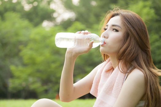 Woman sit and drink after exercise. On the lawn after a workout in the park.