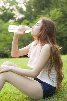 Woman sit and drink after exercise. On the lawn after a workout in the park.