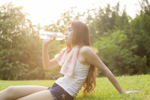 Woman sit and drink after exercise. On the lawn after a workout in the park.