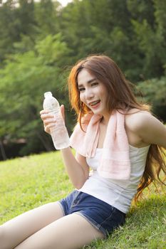 Woman sitting rest after exercise. Hand holding a bottle of water and sit On the lawn.