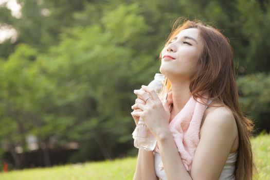 Woman sitting rest after exercise. Hand holding a bottle of water and sit On the lawn.